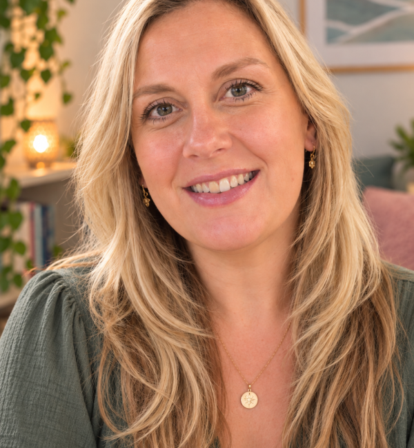 Terri Fowler smiling, with long blonde hair, a green top and a gold pendant necklace, in a room with plants